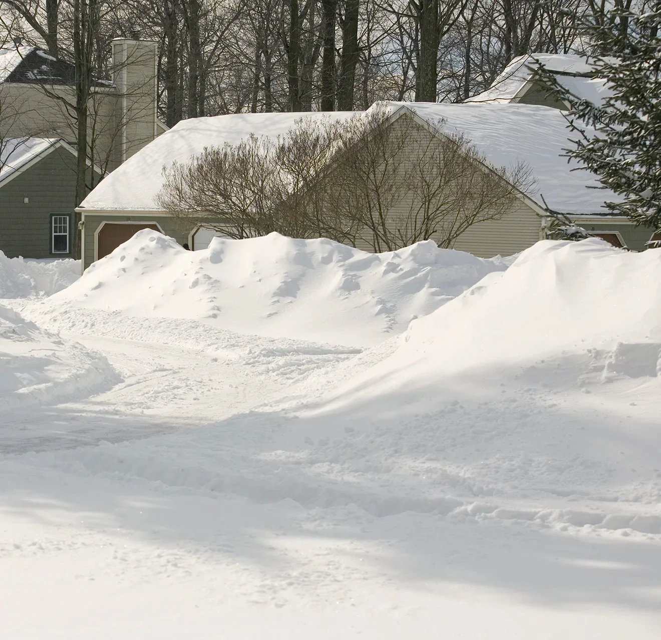 Snow plowed off a residential road and piled high at the end of a home's driveway.