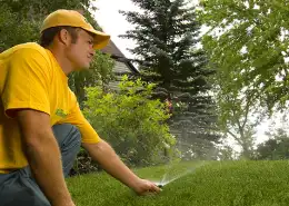 Landscaper inspecting a sprinkler system watering a green lawn.