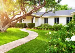 Curved garden path and landscaped front yard outside a home with trees and flowers.